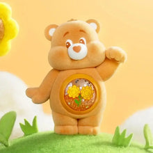 Une figurine nounours câlin tan en peluche avec fenêtre ronde sur le ventre montrant des tournesols pailletés boîte mystère