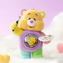 Figurine nounours câlin jaune avec gilet violet et pantalon vert tenant une palette et un crayon dans une boîte mystère pop mart