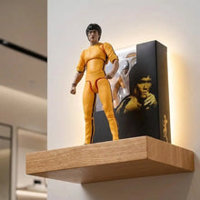 Figurine bruce lee legacy 50th jaune en tenue darts martiaux ajustée avec bordure noire sur étagère en bois à côté du packaging