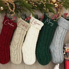 Cinq chaussettes de noël tricotées personnalisables en rouge beige crème vert et gris suspendues à une guirlande festive