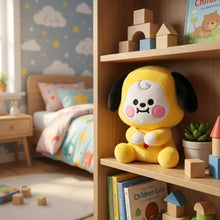 Peluche compagnon pop jaune en tissu peluche avec oreilles noires et joues roses posée sur une étagère en bois