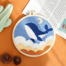 Kit de broderie punch needle avec motif de baleine bleue et blanche sautant parmi des nuages sur fond ciel bleu