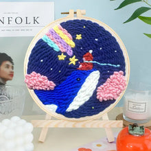 Kit de broderie punch needle montrant un motif décoratif baleine bleue avec nuages roses et étoiles sur fond marine