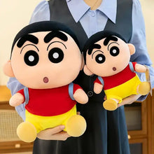 Peluche écolier espiègle shin-chan avec visage beige, sourcils noirs, chemise rouge, short jaune et sac à dos