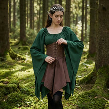 Une elfe médiévale porte une cape à manches longues vert foncé sur une robe marron avec un corset à lacets pour fêtes médiévales