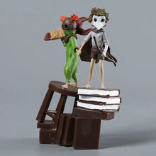 Deux figurines stylisées little nightmares iii en vert avec chapeau plumé rouge et masque de médecin en cape brune sur tabouret en bois