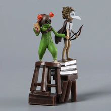 Figurines little nightmares iii vertes et brunes sur un tabouret en bois miniature posé sur des livres empilés