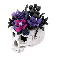 Lego moc crâne blanc en jardinière rempli de fleurs en plastique violettes, roses et bleu marine avec baies noires
