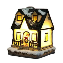 Maisonnette lumineuse de noël miniature à piles avec toit noir enneigé, fenêtres jaunes lumineuses et couronne festive