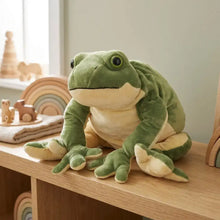 Une peluche géante grenouille verte avec un ventre crème et des yeux noirs posée sur une surface en bois