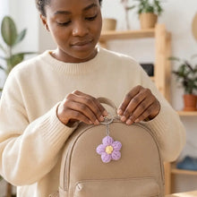 Porte-clés fleur tricotée lavande avec centre jaune en chaîne argentée suspendu à un sac à dos beige
