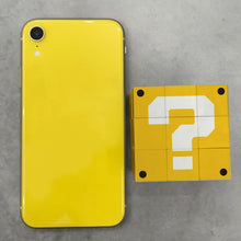 Smartphone iphone xr jaune vif avec finition brillante à côté d’un rubik’s cube bloc point d’interrogation mario jaune