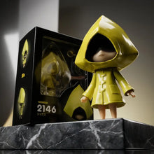 Figurine six little nightmares imperméable jaune brillante 9,5 cm avec capuche et boutons à côté de son emballage noir