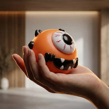 Squishy chien à visage interchangeable orange avec une grande œil veinée entourée de pics noirs et dents blanches