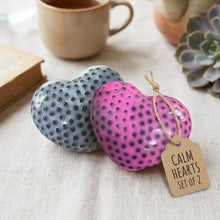 A set of two textured ceramic squishy anti-stress cœur in vibrant pink and muted gray with dark dot patterns