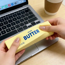 Squishy en forme de beurre jaune salé 113g avec lettres bleues tenu au-dessus d’un ordinateur portable pour magasins de jouets