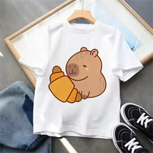 T-shirt blanc en coton avec un motif capybara marron tenant un croissant orange, disponible pour enfant et adulte