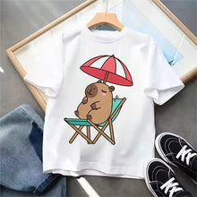 T-shirt blanc capybara en coton avec illustration dessin animé capybara sous parasol rayé rouge et blanc sur chaise de plage