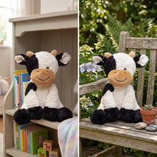 Une peluche vache douce noire et blanche avec un visage beige assise sur une surface en bois compagnon sourire